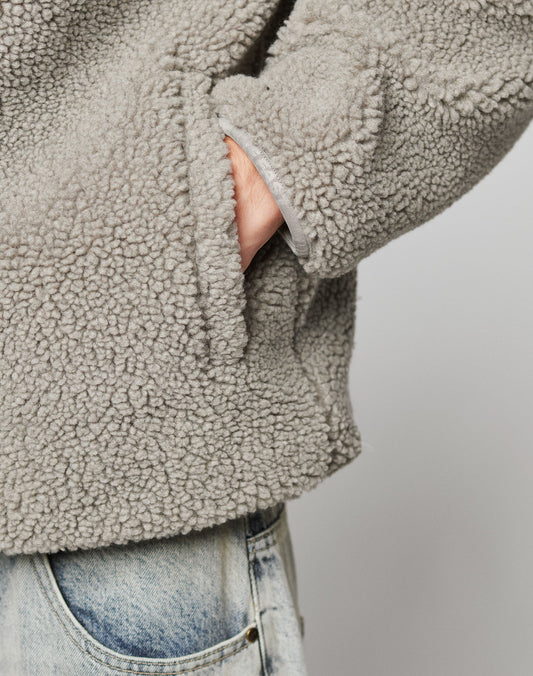 A person wearing the LIVE FAST DIE YOUNG Live Fast Teddy Jacket in light gray sherpa fleece, with one hand in the side pocket, paired with light blue jeans and subtle embossed branding, stands against a plain background.