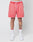 A person wears LIVE FAST DIE YOUNG Basic Sweat Shorts in coral pink with an elastic waistband and handcrafted fade effect, white socks with red accents, and white sneakers. Only their lower body is visible against a plain light background.