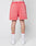A person faces away, wearing LIVE FAST DIE YOUNG Basic Sweat Shorts in coral pink with elastic waistband and handmade fade effect, plus white socks with red trim and white sneakers, set against a plain light background.
