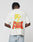 A person with short, twisted hair faces away wearing the LFDY Flash Tee by LIVE FAST DIE YOUNG—an oversized white t-shirt with a bold back graphic: a large yellow lightning bolt over “LIVE FAST” in red and yellow, plus green accents.