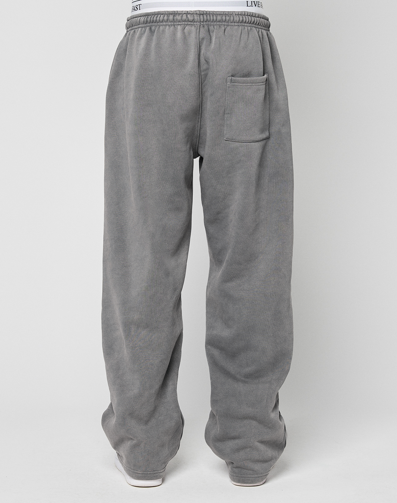 A person wears LIVE FAST DIE YOUNG's Basic Wide Jogger—oversized fit, gray sweatpants with an elastic waistband and one back pocket—standing against a white background, showing only the lower half of the body.