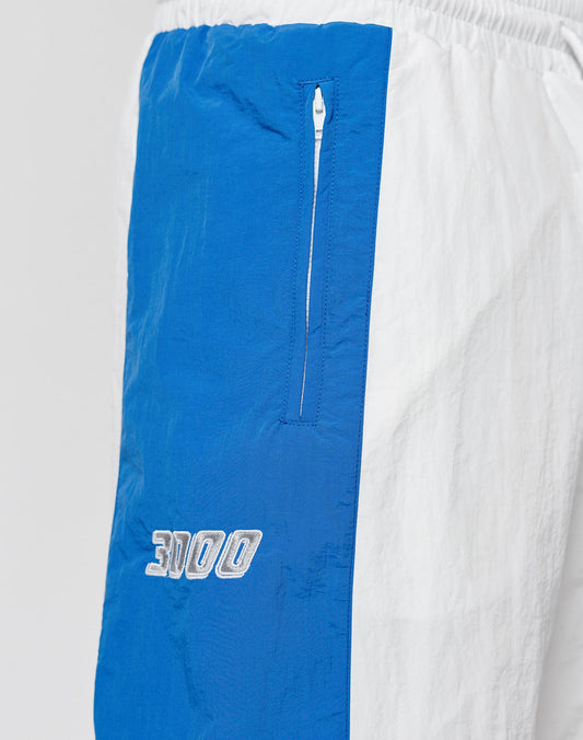 Close-up of LIVE FAST DIE YOUNG LFDY Trackpants 3000, showcasing a vertical blue panel with zippered pocket, white 3000 embroidery, and elastic waistband against a white background.