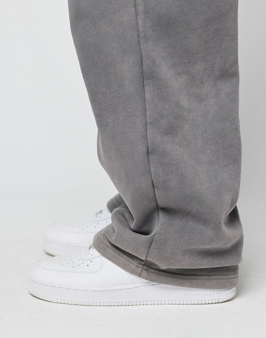 Someone stands against a plain light background wearing LIVE FAST DIE YOUNGs Basic Wide Jogger—loose-fitting gray pants with an elastic waistband and drawstring—that cover the tops of white sneakers.