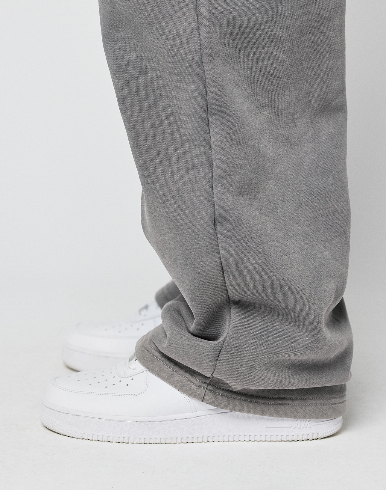 A close-up side view of a person wearing the LIVE FAST DIE YOUNG Basic Wide Jogger in gray, featuring an oversized fit that drapes over white sneakers, set against a plain white background.