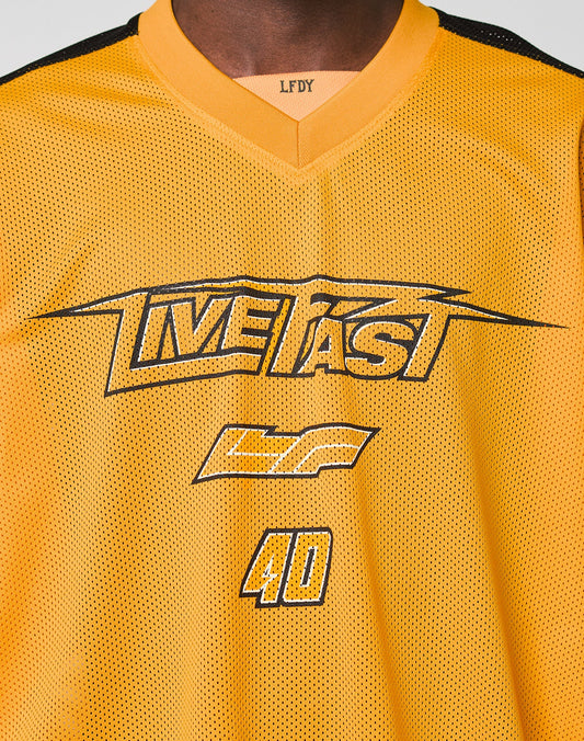 A close-up of a person wearing the LFDY Autobahn Jersey by LIVE FAST DIE YOUNG, featuring a yellow mesh polyester fabric, oversize fit, black “LIVE FAST” and “GF 40” prints on the front, and multilogo details including LFDY on the neckline.