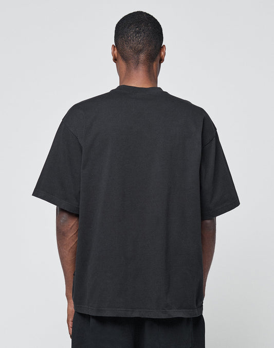 A person with short hair is shown from behind, wearing a LIVE FAST DIE YOUNG Basic Heavy Tee in black and black pants against a light gray background.