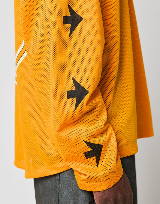 A person wears the LFDY Autobahn Jersey by LIVE FAST DIE YOUNG—an orange oversized polyester mesh long-sleeve shirt with three black arrow symbols on the sleeve—paired with dark pants against a plain light background.