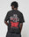 A person with short, twisted hair wears the LFDY We Walked Tee by LIVE FAST DIE YOUNG: an oversized black 100% cotton T-shirt with bold white and red WE WALKED SO THEY CAN RUN front/back prints, flame graphics, and BE YOUNG FOREVER at the bottom.