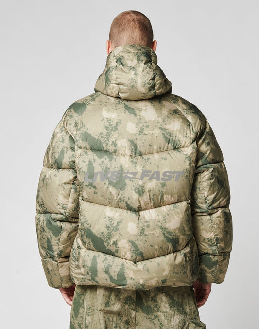 A person seen from behind wears the LIVE FAST DIE YOUNG Live Fast Puffer Jacket in green and beige camo with a hood and a subtle reflective WESTFAST backprint, paired with matching camouflage pants.