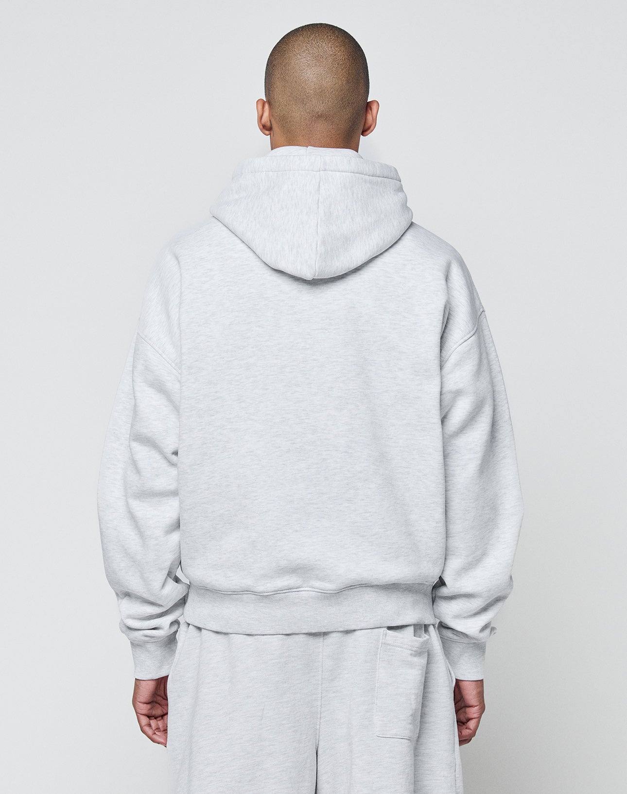 A person with a shaved head, seen from behind, wears the LIVE FAST DIE YOUNG Basic Blank Hooded sweatshirt and matching sweatpants in light gray against a plain backdrop.
