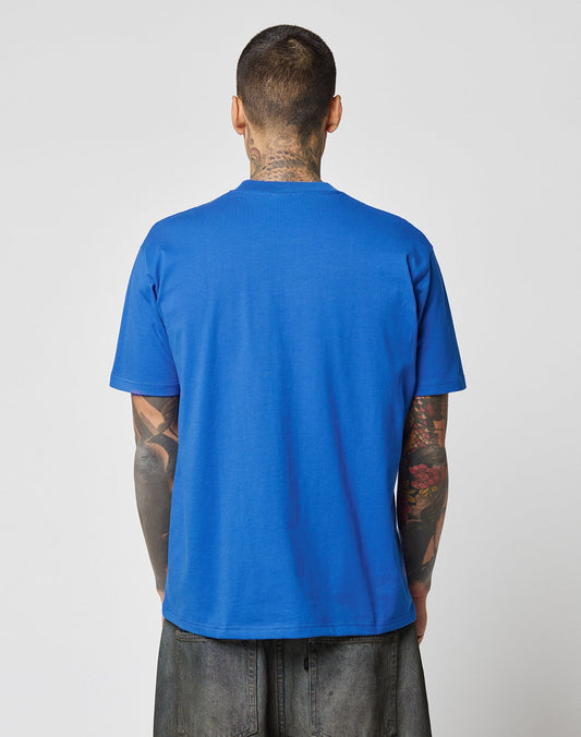 A tattooed person stands with their back to the camera, wearing the LIVE FAST DIE YOUNG LFDY Crash Kid Tee and loose dark pants against a light gray background.