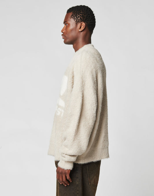 A man in profile faces left against a plain background, wearing the LIVE FAST DIE YOUNG Live Fast Fuzzy Sweater in oversize light beige with dark pants. His arms are relaxed at his sides.