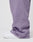 A close-up side view shows a person wearing LIVE FAST DIE YOUNG Basic Wide Jogger pants in lavender with a Wide Fit and elastic waistband, paired with white sneakers, standing on a white surface against a plain background.