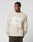 A man in the LIVE FAST DIE YOUNG Live Fast Fuzzy Sweater, featuring a bold intarsia logo, polyamid-elastan mix, oversize fit, and light beige color, stands against a plain background looking to his left.