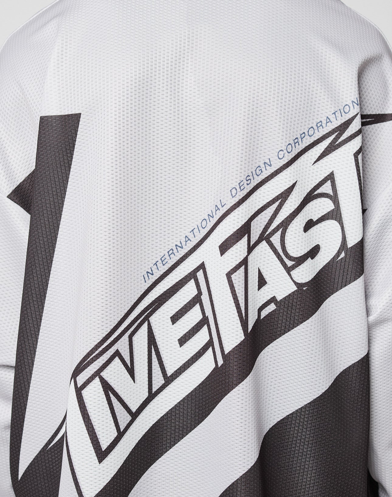A close-up of the LFDY Racetrack Jersey by LIVE FAST DIE YOUNG shows its white polyester mesh with bold black “LIVE FAST” text and smaller blue “INTERNATIONAL DESIGN CORPORATION” above, designed in an oversized fit.