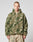 A person with short hair wears the LIVE FAST DIE YOUNG Live Fast Teddy Jacket—an oversize fit, fuzzy, camouflage-patterned piece with a hood and visor opening—paired with loose, light pants against a plain light background.