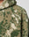 Close-up of a person wearing the LIVE FAST DIE YOUNG Live Fast Teddy Jacket in green and beige with fuzzy, camouflage-like sherpa fleece and embossed branding. Visible: upper chest, shoulder, and partial hood with visor opening.