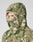 A person wears the LIVE FAST DIE YOUNG Live Fast Teddy Jacket in beige and green camo, featuring a hood with visor opening that reveals part of their face. Subtle embossed branding accents the fleece, set against a light gray background.