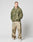 A person stands against a plain background wearing the LIVE FAST DIE YOUNG Live Fast Teddy Jacket in green camouflage with Kapuze mit Visor-Öffnung, loose beige camo pants, and white sneakers, hands in pockets and looking to the side.