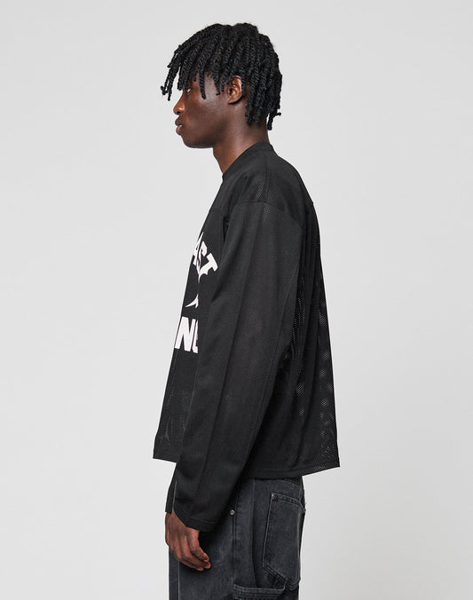 A person with short, twisted hair stands in profile wearing the LIVE FAST DIE YOUNG LFDY Flash Jersey—an oversize black long-sleeve mesh shirt with a bold front print and white text—paired with black jeans against a light gray background.