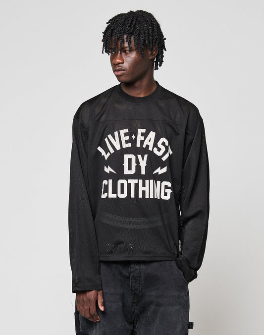 A person with short, twisted hair wears an oversized black LFDY Flash Jersey by LIVE FAST DIE YOUNG, featuring a bold white front print, standing against a plain light background.