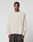 A person stands facing forward against a plain light background, wearing the cream-colored LIVE FAST DIE YOUNG LFDY Praying Fuzzy Sweater with an oversize fit and dark, loose-fitting pants.