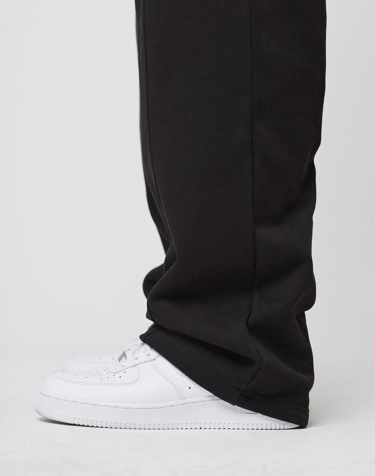 A person wearing LIVE FAST DIE YOUNG Basic Wide Jogger—wide fit, black, soft cotton, with elastic waistband—partially covering white sneakers, stands against a plain white background.