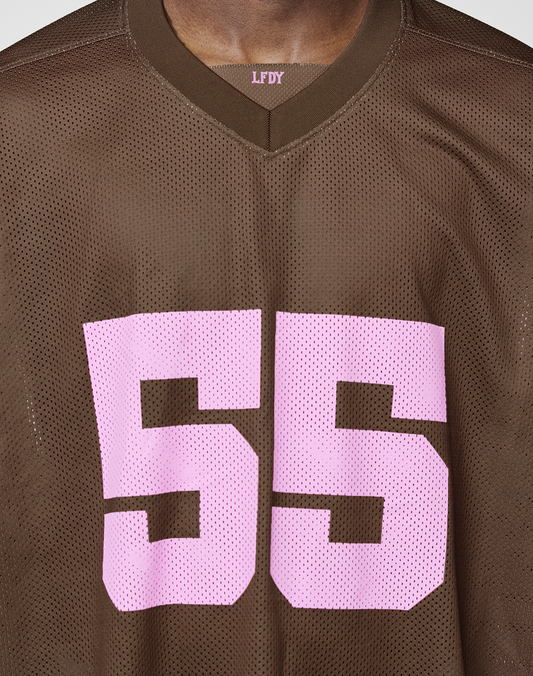 A close-up of the LFDY Mesh Jersey by LIVE FAST DIE YOUNG shows a brown oversized mesh polyester sports top with a pink '55' on the front, a V-neckline with LFDY inside, and part of the model's neck and face visible.