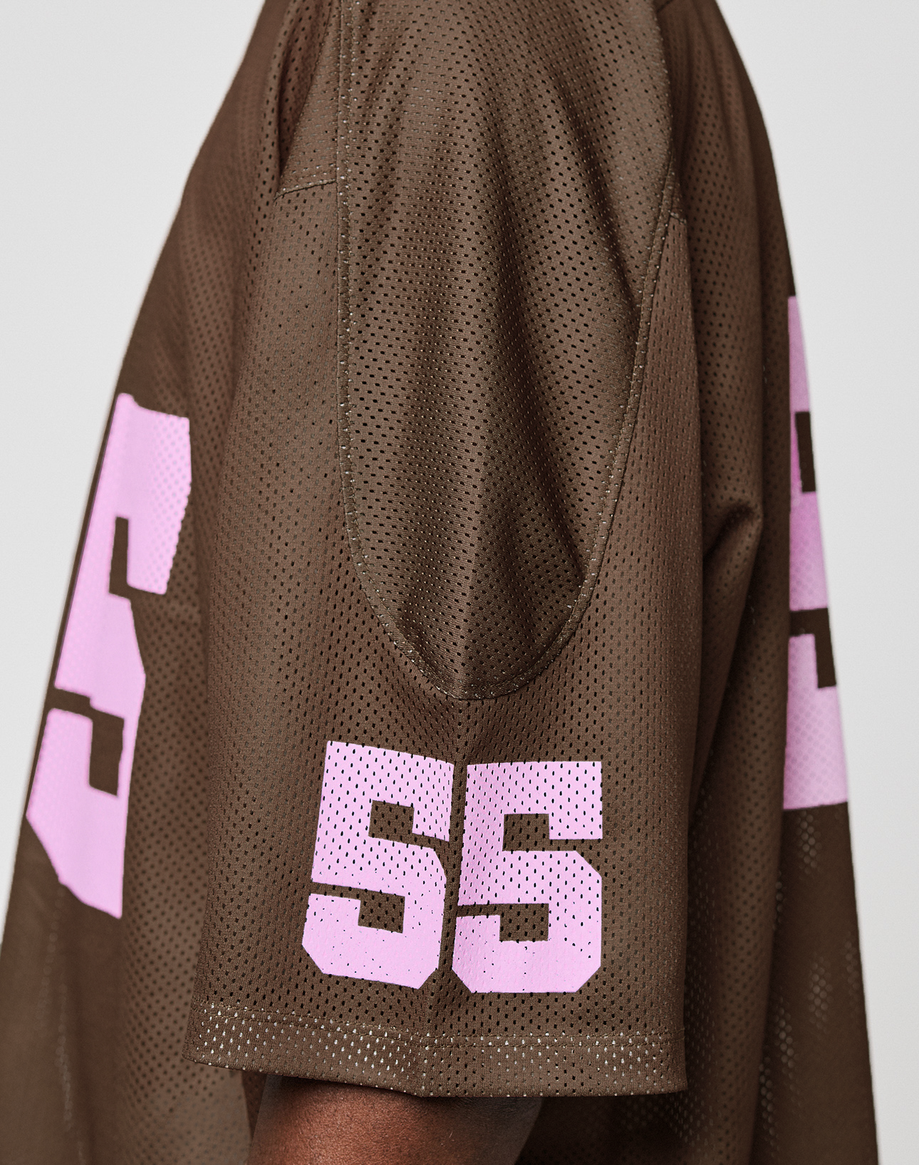 A person wears the LFDY Mesh Jersey by LIVE FAST DIE YOUNG, featuring an oversize brown mesh design with pink numbers 55 on the sleeve and a partially visible 5 on the back. Only the right side of their upper body and arm is shown.