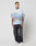 A tattooed man wears a LIVE FAST DIE YOUNG LFDY Crash Kid Shirt in light blue (oversize fit, short sleeves, logo print), paired with loose dark jeans and white sneakers, standing against a plain white background.