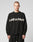 A person with short hair models the LIVE FAST DIE YOUNG Live Fast Boucle Sweater—an oversize black polyester piece with LIVE FAST in bold white across the chest—against a plain light gray background.