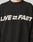 A person wears the Live Fast Boucle Sweater by LIVE FAST DIE YOUNG—an oversized black piece with LIVE FAST and a fast-forward arrow in bold white, crafted from soft Strick polyester for comfort and style.