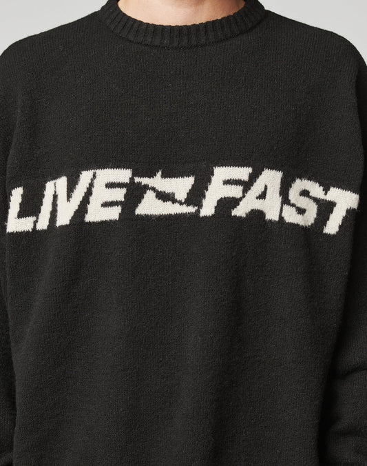 A person wears the Live Fast Boucle Sweater by LIVE FAST DIE YOUNG—an oversized black piece with LIVE FAST and a fast-forward arrow in bold white, crafted from soft Strick polyester for comfort and style.