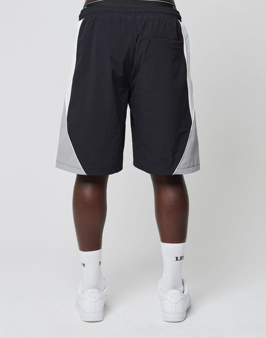 A person faces away from the camera wearing LIVE FAST DIE YOUNG Basic Nylon Trackshorts, white crew socks with LFE logo-stick detail, and white sneakers against a plain light background.