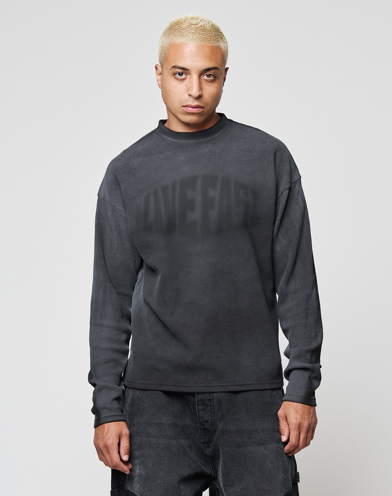 A person with short blond hair wears the LIVE FAST DIE YOUNG LFDY Emblem Ghost Waffle Longsleeve and dark pants, standing against a plain light background and looking directly at the camera with a neutral expression.
