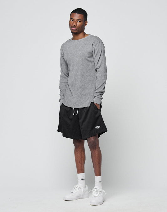 A person stands against a plain background, wearing the LIVE FAST DIE YOUNG Basic Regular Rib Longsleeve in gray, paired with black shorts, white socks, and white sneakers in a regular fit, hands in pockets and a relaxed expression.