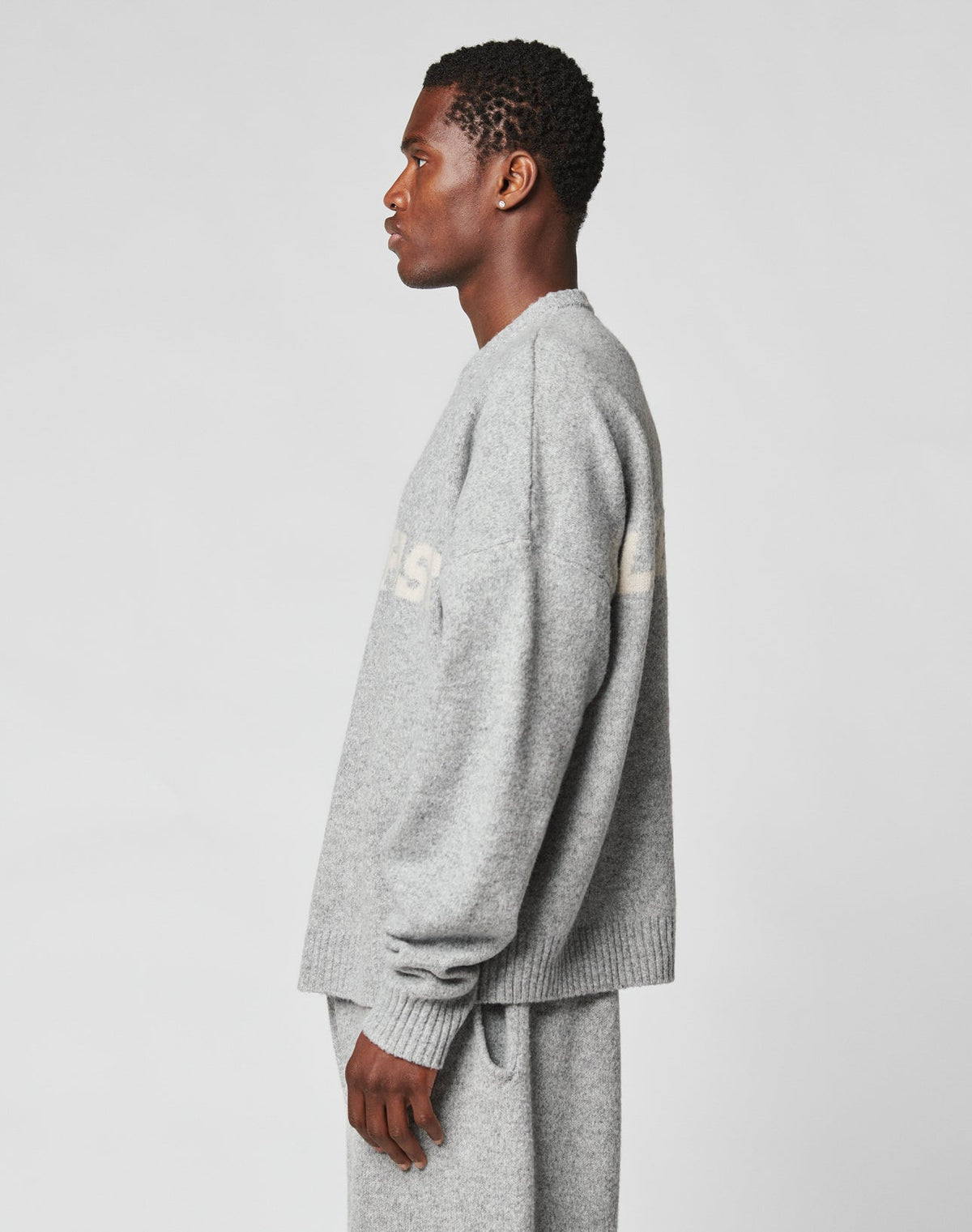 A man in profile faces left, wearing the Live Fast Boucle Sweater and matching gray pants by LIVE FAST DIE YOUNG, both loose-fit and 100% polyester, set against a plain light background.