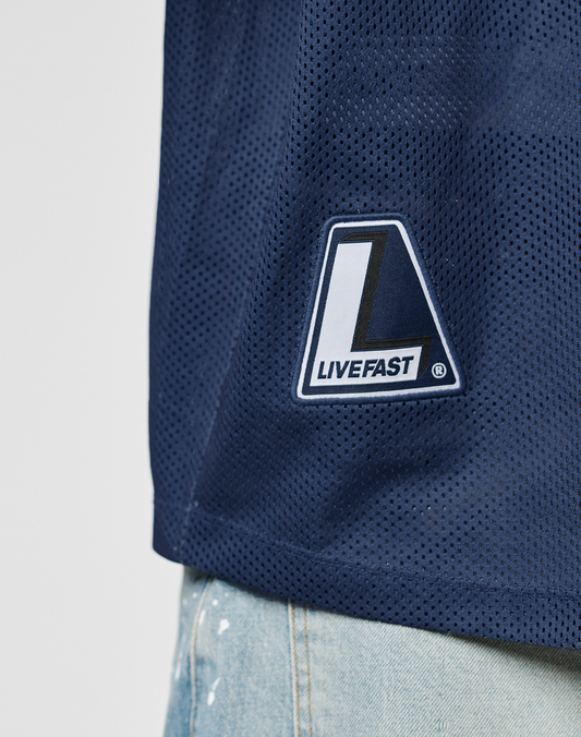 Close-up of the LFDY Mesh Jersey by LIVE FAST DIE YOUNG in dark blue, oversize fit with a V-neck and LIVEFAST patch, styled with light blue jeans featuring white paint splatters. Made from breathable polyester for comfort and style.