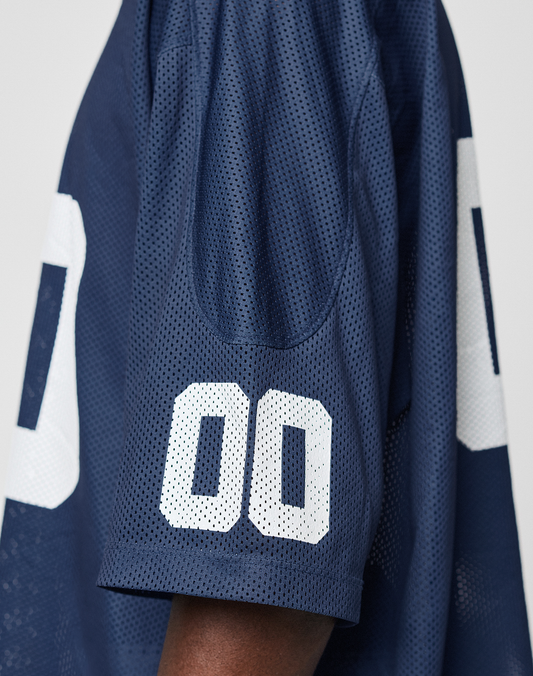 A close-up of the LIVE FAST DIE YOUNG LFDY Mesh Jersey in dark blue polyester shows white mesh “00” on the sleeve and body, with a visible arm highlighting its casual oversized fit.