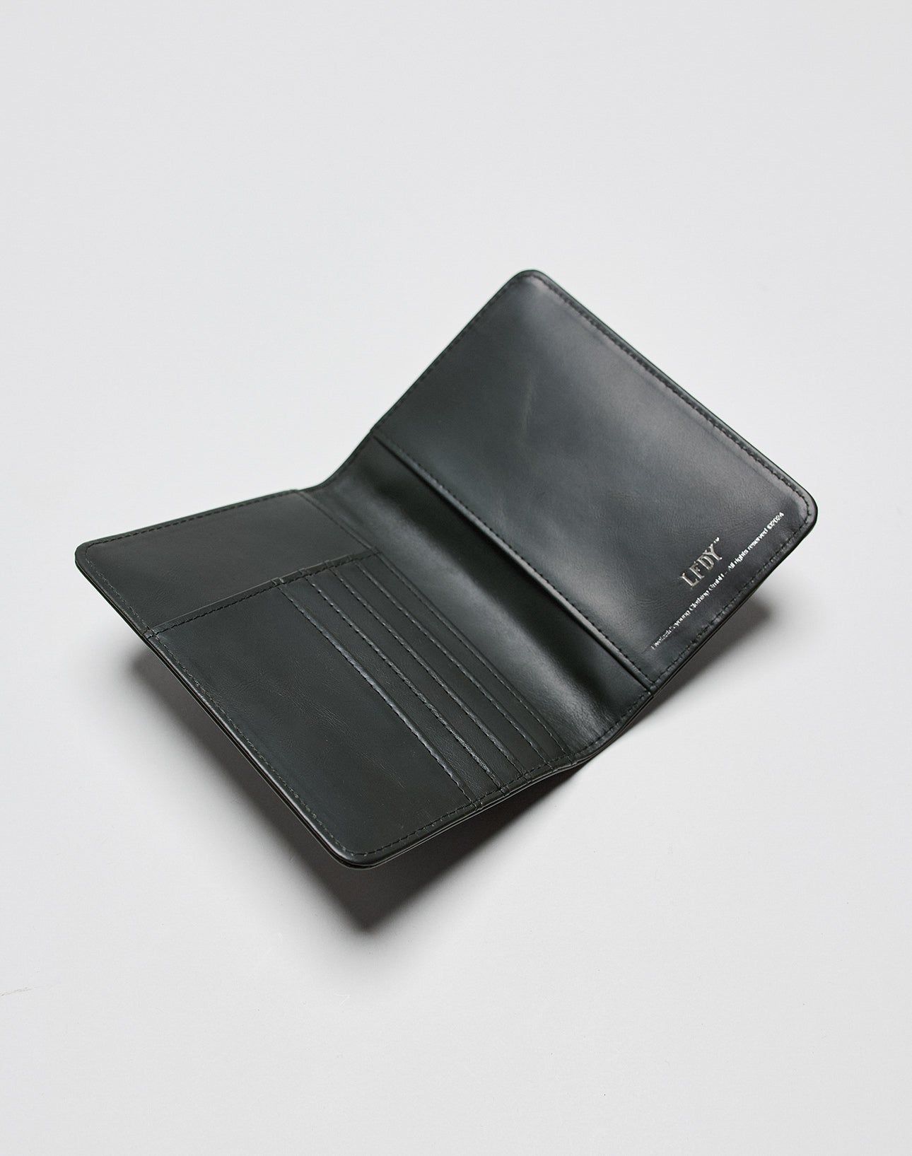 A black LFDY Passport Case by LIVE FAST DIE YOUNG, featuring multiple card slots and a bill section, is displayed open on a light gray surface. The word LUFF appears embossed in silver on the right side.