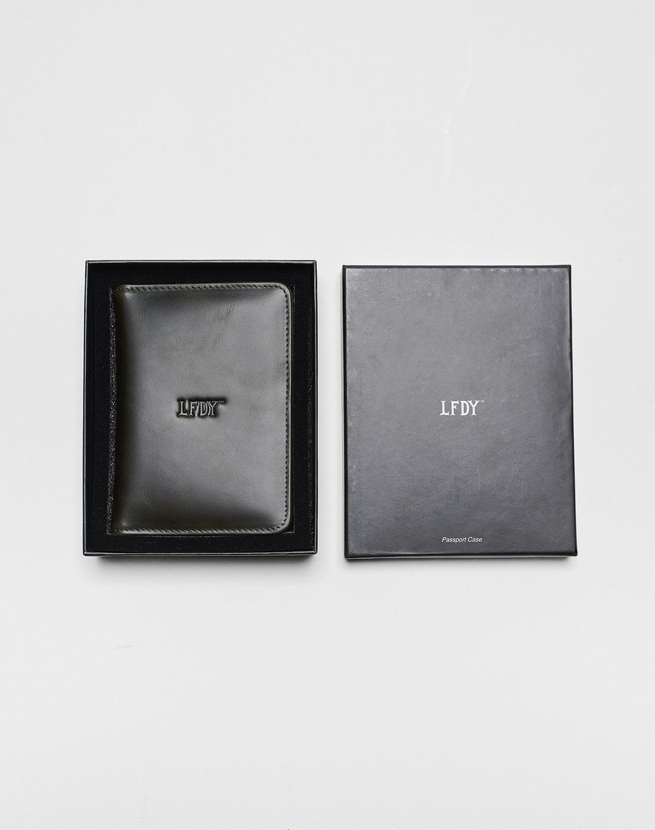 Die LFDY Passport Case von LIVE FAST DIE YOUNG aus schwarzem Leder zeigt „LFDY“ auf der Vorderseite und wird in einer offenen schwarzen Box mit Logo und „Passport Case“ geliefert. Innen sorgen Kartenfächer für Ordnung.