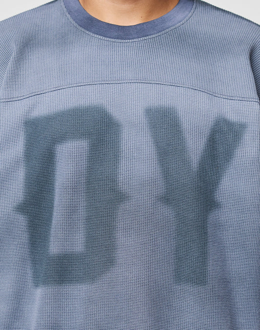 Close-up of a person wearing the LIVE FAST DIE YOUNG Faded Waffle Jersey, an oversized, textured blue shirt made from 100% Baumwolle with large blurred DY letters on the faded front; only neck and upper torso are shown.