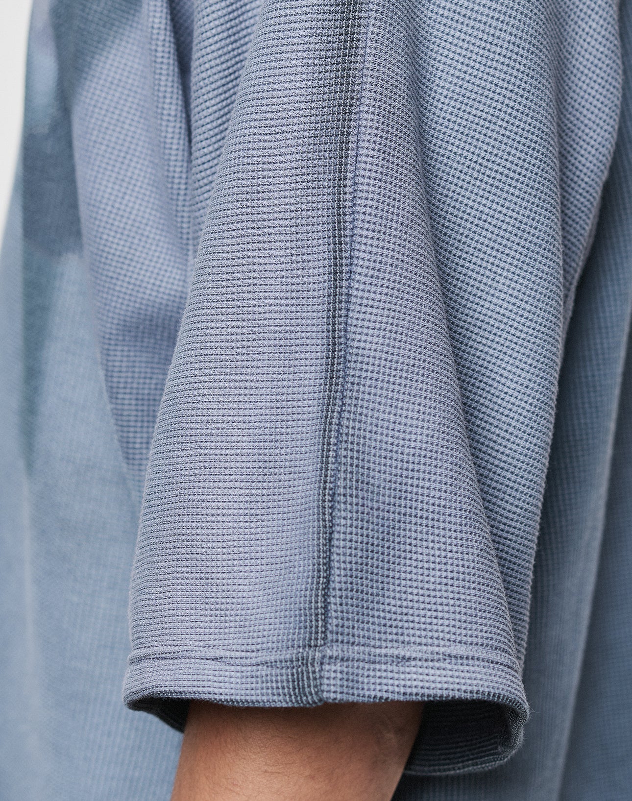 Close-up of a person’s arm in the LIVE FAST DIE YOUNG Faded Waffle Jersey, featuring light blue textured 100% Baumwolle fabric and an Oversize Fit. Only part of the shirt and arm are visible, showcasing its modern comfort and style.