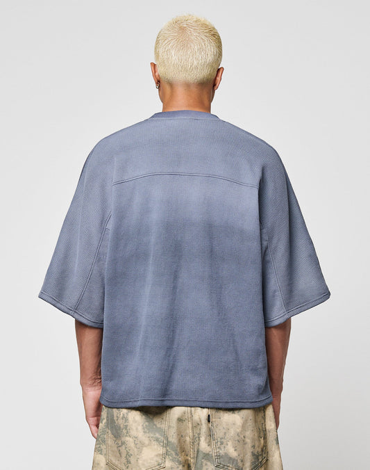 A person with short, bleached blonde hair is shown from the back wearing the LIVE FAST DIE YOUNG Faded Waffle Jersey, an oversize fit faded blue shirt made of 100% Baumwolle, paired with light patterned pants against a plain background.