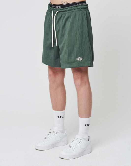A person wearing LIVE FAST DIE YOUNG Basic Mesh Shorts in green, white crew LFDY socks, and white Nike sneakers stands against a plain white background. Only the lower body is visible. | model