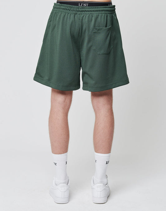 A person is shown from the waist down wearing LIVE FAST DIE YOUNG Basic Mesh Shorts in green with an elastic waistband, LJST branding, a back pocket, white socks, and white sneakers. The background is plain white.