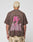 A person with short bleached blond hair is seen from behind, wearing the LFDY Flash Tee by LIVE FAST DIE YOUNG—an oversized brown cotton-slab shirt with a bold pink lightning bolt and LIVE FAST backprint—paired with tan camo shorts.
