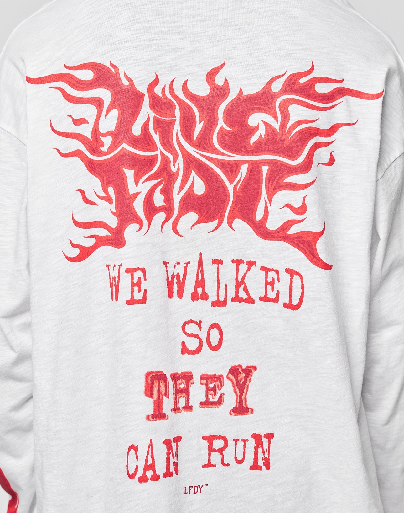 The LFDY We Walked Longsleeve by LIVE FAST DIE YOUNG is a white cotton-slub shirt with a red flame UNITY graphic and WE WALKED SO THEY CAN RUN. LFDY text. Oversize fit ensures added comfort.