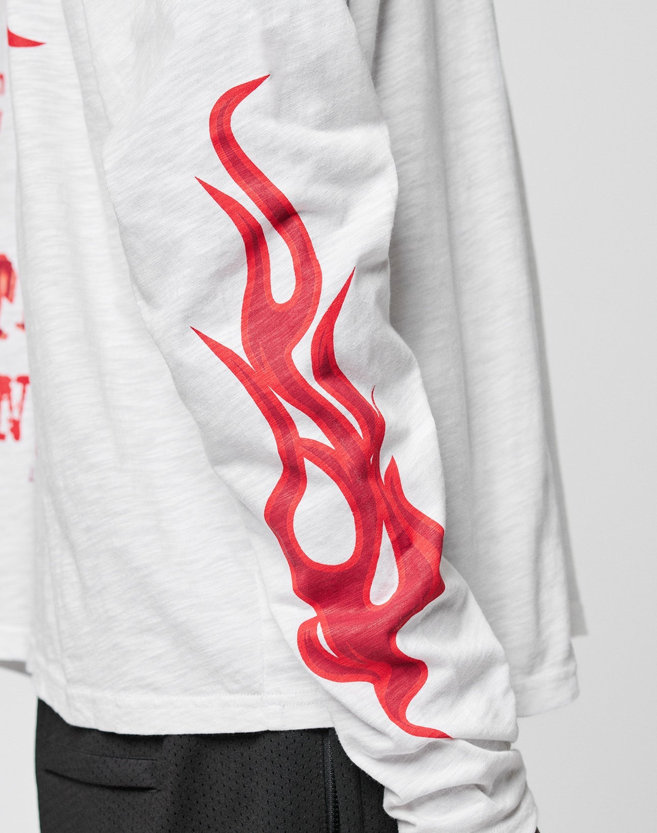 A close-up of the LIVE FAST DIE YOUNG LFDY We Walked Longsleeve in white Oversize Fit, featuring a bold red flame graphic down the sleeve. Black shorts are partially visible at the bottom of the image.