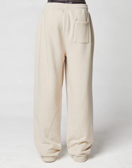 The LFDY Pleated Jogger by LIVE FAST DIE YOUNG is a wide-fit, cream sweatpant made of soft cotton with an elastic waistband and a patch pocket on the left thigh, modeled against a plain white background.